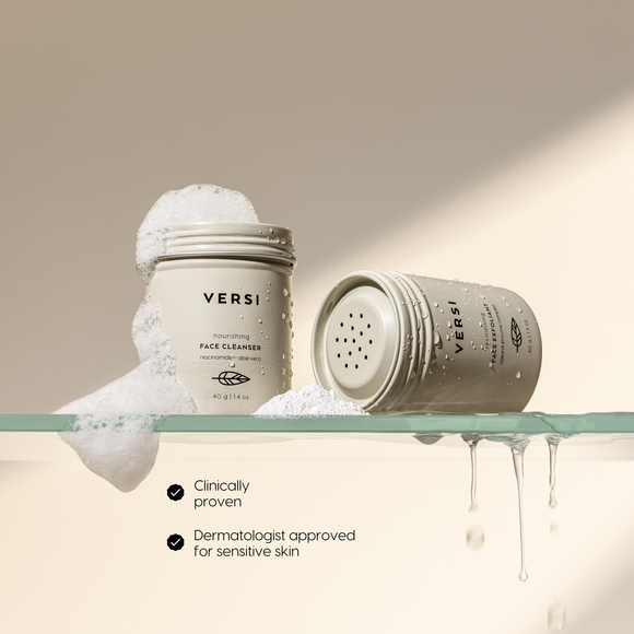 Versi face cleanser and exfoliant jars on a glass shelf with foam and water droplets,  on a warm beige background.