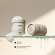Versi face cleanser and exfoliant jars on a glass shelf with foam and water droplets,  on a warm beige background.
