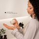 A woman in a bathroom holds a small skincare jar and pours the powder contents onto her hand. Text on the mirror reads 'Lasts 200 uses (6-7 months with daily use)'.
