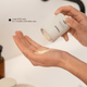 A close-up of a hand holding a beige container and pouring a pale yellow cleansing powder into another hand. The container has black text reading 'VERSI' and 'Face Cleanser'.