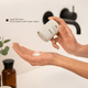 Person holding a beige container labeled 'Versi Face Exfoliant' over their palm with a blurred background.