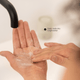 A close-up of a hand lathering under a faucet, with a second hand applying a exfoliant. A small text overlay reads 'Easily melts into a light lather'.