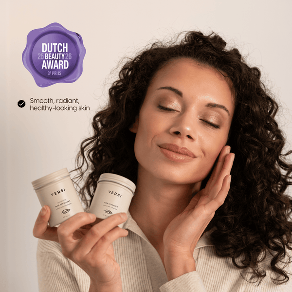 A woman with curly dark hair holds two beige jars branded VERSI, showing how the powder skincare gives her soft, radiant skin. She is shown against a soft light beige background a purple award badge reading Dutch Beauty Award 2025/2026.