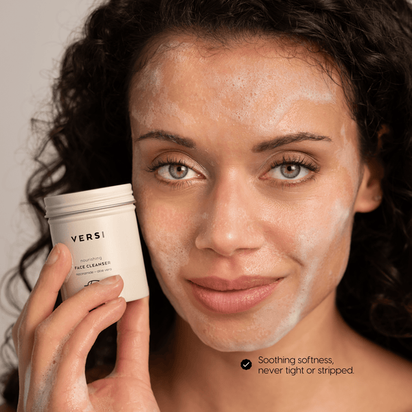 A close-up of a woman Chantal van Dalen with a foaming facial cleanser applied to her face, holding a beige jar labeled Versi. The text at the bottom right reads 'Soothing softness, never tight or stripped.