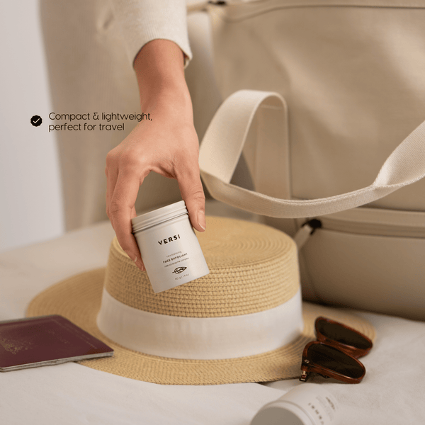 A hand holds a compact beige cosmetic jar labeled Verst over a beige travel bag, with a straw hat, sunglasses, and a passport nearby. Text on the image reads 'Compact & lightweight, perfect for travel'.